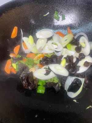 副菜の炒め物：フライパンに油を少し残し、さらに油を加えて、ニンニクのスライスとショウガのスライスを香りが立つまで炒め、次にピーマン、ニンジン、タマネギ、キクラゲを加えて、副菜に火が通るまで炒めます。