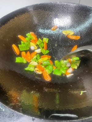 副菜の炒め物：フライパンに油を少し残し、さらに油を加えて、ニンニクのスライスとショウガのスライスを香りが立つまで炒め、次にピーマン、ニンジン、タマネギ、キクラゲを加えて、副菜に火が通るまで炒めます。