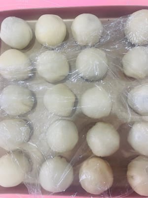 Preparazione per l'involucro
Stendete l'impasto e arrotolatelo in una forma rotonda. Avvolgetelo con la pasta di fagioli rossi e il ripieno di tuorlo d'uovo. Premete con il palmo della mano. Posizionatelo sulla teglia con la chiusura rivolta verso il basso. Prestate attenzione alla spaziatura. Coprite con pellicola trasparente per mantenerlo umido.