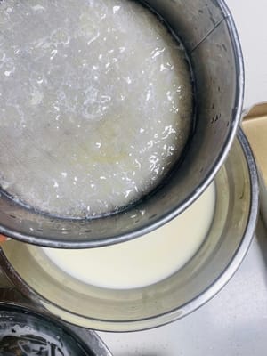かき混ぜたエッグタルト液を篩に注ぎ、スプーンで押して濾し、液が篩を通過して下の容器に移ります。1回目の濾過後、容器内のエッグタルト液を再び篩に戻し、2回目の濾過を行います。