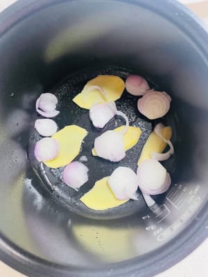 电饭煲内喷一层薄油，启动“煮饭”模式预热，放入洋葱丝和姜片。