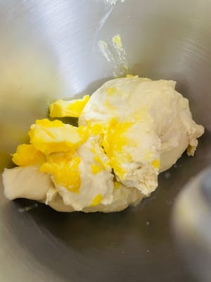 Tambahkan mentega yang sudah dilunakkan dan uleni hingga adonan dapat diregangkan menjadi membran tipis dan tembus cahaya (membran sempurna). Jika menguleni dengan tangan, gunakan metode melipat dan metode rendaman air. Pengingat penting: Suhu adonan tidak boleh melebihi 23°C setelah dikeluarkan dari mangkuk pengaduk. Jika terlalu panas, gunakan susu dingin, dan Anda juga dapat mengikat kantong pendingin di sekitar mangkuk pengaduk untuk mencegah adonan mengalami 