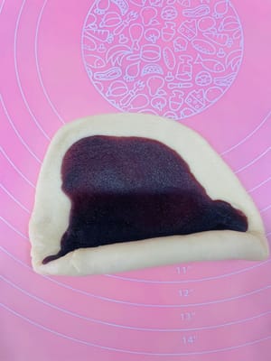 Ambil bola adonan yang sudah rileks, giling hingga berbentuk lembaran bulat, oleskan tipis pasta kacang merah di atasnya, gulung, giling sedikit lebih tipis, dan gulung lagi. Dengan cara ini, isian pasta kacang merah dapat tersebar lebih merata, tidak seperti saat membuat bakpao yang menggumpal di tengah dan terlalu manis saat digigit.