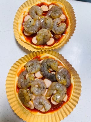 Pizza Sosis dan Udang Cara Merakit: Oleskan saus pizza tebal-tebal pada alas pizza mini, beri topping sosis, udang, dan paprika hijau dan merah, lalu tutupi dengan tumpukan keju mozzarella yang tebal. Toppingnya sangat melimpah hingga hampir tumpah!