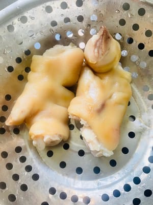 Zuerst die Haare von den Schweinsfüßen abflämmen und diese sauber schaben. Anschließend in einen Topf mit kaltem Wasser, Ingwerscheiben, Kochwein und Sichuanpfeffer geben. Sobald das Wasser kocht, 5 Minuten kochen lassen, dann herausnehmen und gründlich abspülen.