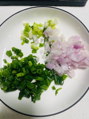 Trennen Sie die weißen und grünen Teile der Frühlingszwiebeln und schneiden Sie sie klein. Hacken Sie die Zwiebel ebenfalls fein, um den Geschmack zu intensivieren.