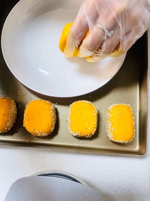 成形したサツマイモの端を水で湿らせ、白ゴマに転がしてしっかりとくっつけます。