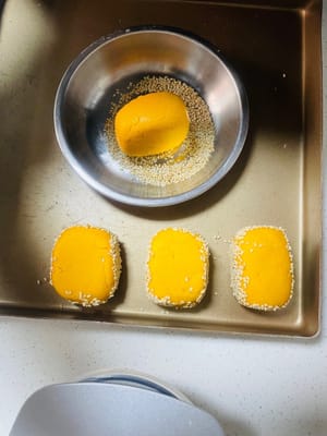 成形したサツマイモの端を水で湿らせ、白ゴマに転がしてしっかりとくっつけます。