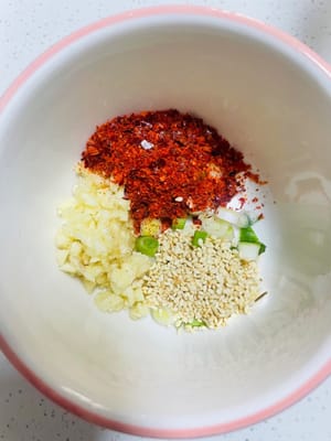 Preparare la salsa soul: preparare una ciotola per condire, aggiungere l'aglio tritato, le foglie bianche di cipollotto tritate, 2 cucchiai di peperoncino in polvere e 1 cucchiaio di semi di sesamo bianchi.