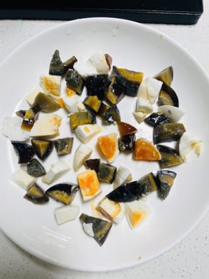 Coloque el huevo salado cortado en cubitos y el huevo conservado en un recipiente humeante y luego vierta lentamente el líquido del huevo colado en el recipiente.