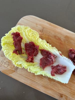 Layer sliced beef onto cabbage as demonstrated