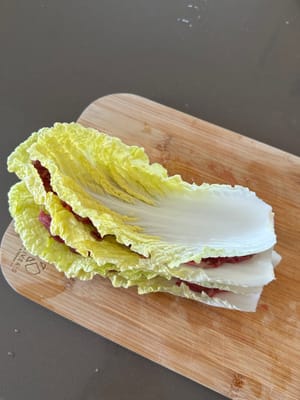 Layer sliced beef onto cabbage as demonstrated