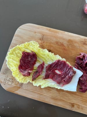 Layer sliced beef onto cabbage as demonstrated