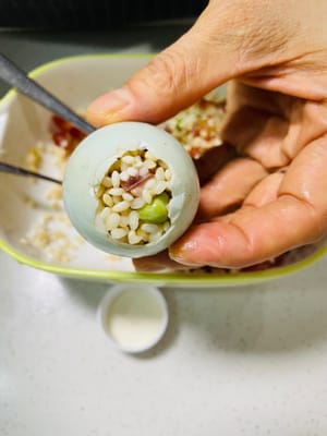 Con una cuchara pequeña, introduzca lentamente el relleno de arroz glutinoso en la cáscara de huevo salada y presione suavemente (sin ser demasiado brusco, ya que la cáscara se romperá). El relleno debe quedar bien apretado para que no se deshaga después de cocerse al vapor y tenga una textura más consistente.