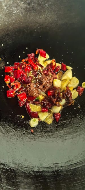 Pour out some of the excess oil. Heat the oil again, then sauté ginger, garlic, and dried chili peppers until fragrant. Add a spoonful of dry pot sauce, a teaspoon of light soy sauce, a little oyster sauce, and a pinch of salt.