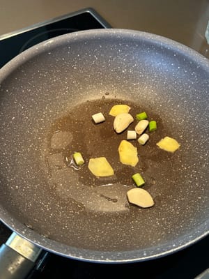 In einer erhitzten Pfanne beginnen Sie mit dem Braten von Frühlingszwiebeln, Ingwer und Knoblauch in Sesamöl