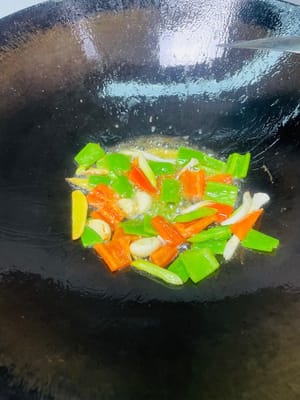 Tumis bahan-bahan: Dengan menggunakan minyak sisa menggoreng perut babi di wajan, tumis siung bawang putih, irisan jahe, dan akar tunas bawang putih hingga harum, lalu tambahkan paprika hijau dan merah dan tumis selama 1 menit.