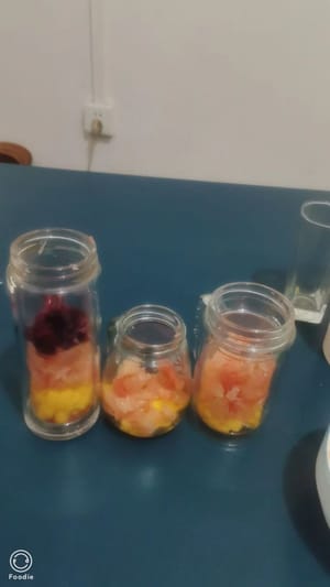 Los geht's mit dem Zusammensetzen! Zuerst eine Schicht Mangostücke auf den Boden geben, dann eine Schicht Grapefruit hinzufügen und die untere Hälfte der Flasche mit Milch füllen, um das Fruchtfleisch zu halten.