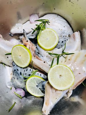 Nachdem Sie den Fischkopf herausgenommen haben, verteilen Sie Rosmarin (reiben Sie ihn sanft, um das Aroma freizusetzen), schwarzen Pfeffer, Zitronenscheiben (pressen Sie etwas Saft aus), etwas Salz und Zwiebelstreifen gleichmäßig auf dem Fischkörper und lassen Sie ihn 15 Minuten lang marinieren.