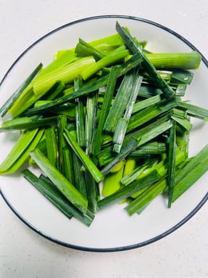 Lavar los brotes de ajo, separar las partes blancas y verdes de los ajos y cortarlos en trozos, luego reservar.