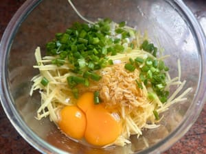 Ajoutez les œufs, les oignons verts, le sel, le poivre noir et l’huile de sésame aux pommes de terre râpées.