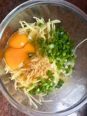 Aggiungere alle patate grattugiate le uova, i cipollotti, il sale, il pepe nero e l'olio di sesamo.
