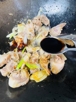 Push the chicken to the side of the wok and add the ginger, garlic, and scallions. Stir-fry until fragrant.
Pour 1 tablespoon of cooking wine from the side of the wok. Add 2 tablespoons of light soy sauce, 1 tablespoon of oyster sauce, 1 tablespoon of dark soy sauce, and the rock sugar. Stir-fry until evenly combined.