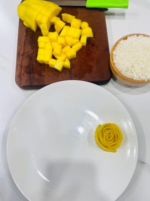 Preparazione del piatto
Tagliate il mango rimanente a pezzetti. Mettete il riso glutinoso imbevuto di latte di cocco in una ciotola da portata, quindi capovolgetelo sul piatto con i fiori di mango. Aggiungete il mango a cubetti e versateci sopra il restante terzo del latte di cocco. Questo piatto di riso glutinoso al mango e latte di cocco è pronto per essere gustato.