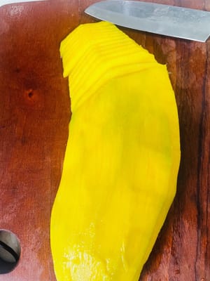 Per preparare i fiori di mango:
Mentre il riso glutinoso assorbe il latte di cocco, preparate i mango. Sbucciate il mango e tagliatelo a fettine sottili per formare i fiori. Per prima cosa, arrotolate la fetta di mango più piccola per formare il centro del fiore. Poi, avvolgete le fette di mango rimanenti attorno al centro, formando un piccolo fiore. Questo creerà un prodotto finito più bello.