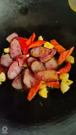 中華鍋に油を熱し、スライスしたニンニクと赤唐辛子を加えて香りが出るまで炒め、刻んだソーセージを加えます。