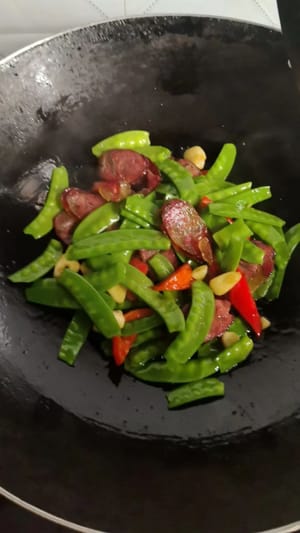 中火でソーセージが透き通るまで炒めます。湯がいたスナップエンドウを加え、火を強めて1分間さっと炒めます。少量の塩で味を調え、再び全体に火が通るまで炒め、火を止めて盛り付けます。