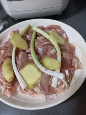 Añade tallos de jengibre y cebolla encima de los muslos de pollo que han sido espolvoreados con pimienta blanca en polvo.