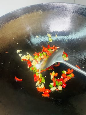 Calienta la sartén a fuego alto, luego reduce el fuego y añade aceite. Primero, sofríe el ajo picado hasta que desprenda un aroma agradable. Luego, añade los chiles picados y espolvorea con una pizca de sal. Remueve bien y reserva.
