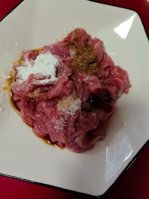 Poner la carne picada en un bol, añadir los condimentos, una cucharadita de salsa de soja ligera, un poco de salsa de ostras, 10 ml de vino de cocina, un poco de sal, un poco de maicena y por último una cucharadita de aceite y mezclar bien.