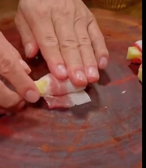 Disporre la pancetta di maiale tagliata a fette su un piatto, adagiare sopra le patatine fritte tagliate a fette e arrotolarle una ad una in questo modo