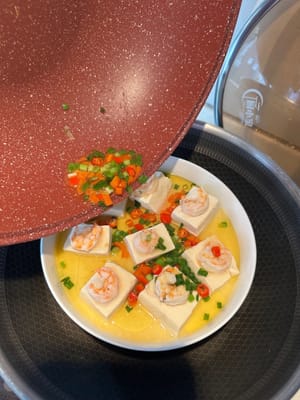 Versare velocemente l'olio caldo, le cipolle e i peperoncini sulle uova e sul tofu.