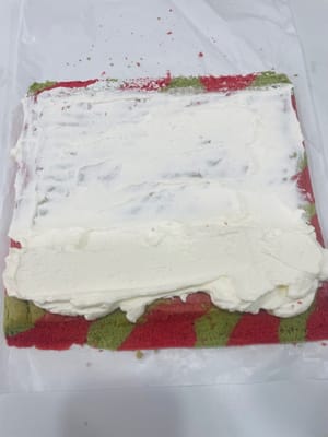 Bestreichen Sie die Ihnen zugewandte Seite des Kuchens mit einer dickeren Schicht Sahne und verteilen Sie die gehackten Erdbeeren darauf. Bestreichen Sie den restlichen Kuchen mit einer dünnen Schicht Sahne. Rollen Sie den Kuchen mithilfe von Backpapier zügig von der Ihnen zugewandten Seite her auf (siehe Video). Wickeln Sie die aufgerollte Biskuitrolle fest in Backpapier ein und stellen Sie sie für 1 Stunde in den Kühlschrank, damit sie fest wird.