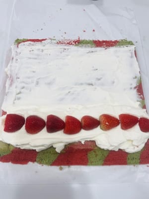 Bestreichen Sie die Ihnen zugewandte Seite des Kuchens mit einer dickeren Schicht Sahne und verteilen Sie die gehackten Erdbeeren darauf. Bestreichen Sie den restlichen Kuchen mit einer dünnen Schicht Sahne. Rollen Sie den Kuchen mithilfe von Backpapier zügig von der Ihnen zugewandten Seite her auf (siehe Video). Wickeln Sie die aufgerollte Biskuitrolle fest in Backpapier ein und stellen Sie sie für 1 Stunde in den Kühlschrank, damit sie fest wird.