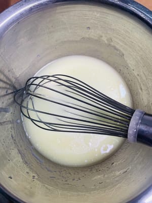 Bereiten Sie den Teig vor. Geben Sie 20 g weißen Zucker, 45 g Maisöl und 45 g Milch in eine Schüssel mit Eigelb und verquirlen Sie die Zutaten, bis eine homogene Emulsion ohne sichtbare Öltropfen entsteht.