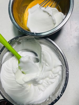 Baiser und Eigelbmasse vermengen
Zuerst ein Drittel des geschlagenen Baisers mit einem Spatel in einer N-förmigen Bewegung unter die Eigelbmasse heben, bis alles gut vermischt ist. Anschließend die Mischung zu den restlichen zwei Dritteln des Baisers geben und erneut in einer N-förmigen Bewegung unterheben, bis alles vollständig vermengt ist und keine weißen Baiserstückchen mehr sichtbar sind.

Durch das Verdünnen der Eigelbmasse vor dem erneuten Unterheben des Baisers wird verhindert, dass dieser zusammenfällt. So kann der Kuchenboden gut aufgehen und die Gefahr von Rissen beim Rollen verringert werden.