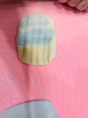 Enrobage de la pâte à base d’huile, premier étalage et repos

Déposez trois portions de 9 g de pâte à base d’huile (ou une portion de 27 g) au centre de la pâte à l’eau, appuyez légèrement avec la paume de la main, puis repliez-la sur elle-même de haut en bas et de gauche à droite. Retournez-la et aplatissez-la délicatement avec un rouleau à pâtisserie, puis tapotez-la avec la main pour uniformiser la pâte à base d’huile et obtenir une surface plus lisse et esthétique. Ensuite, comme pour l’étalage de la pâte à l’eau, roulez-la dans le sens de la longueur, en veillant à ne pas la rouler d’avant en arrière. Retournez-la à nouveau et roulez-la. Ce roulage permet de mieux distinguer les couches de pâte à l’eau et de pâte à base d’huile, ce qui donnera une texture feuilletée plus belle à la cuisson.

Après avoir enrobé toute la pâte à base d’huile avec la pâte à l’eau et l’avoir roulée, laissez reposer 15 minutes. Ce temps de repos est essentiel pour éviter que la pâte ne se déchire si vous la roulez sans cesse.