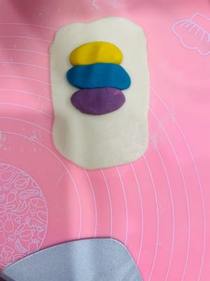 Enrobage de la pâte à base d’huile, premier étalage et repos

Déposez trois portions de 9 g de pâte à base d’huile (ou une portion de 27 g) au centre de la pâte à l’eau, appuyez légèrement avec la paume de la main, puis repliez-la sur elle-même de haut en bas et de gauche à droite. Retournez-la et aplatissez-la délicatement avec un rouleau à pâtisserie, puis tapotez-la avec la main pour uniformiser la pâte à base d’huile et obtenir une surface plus lisse et esthétique. Ensuite, comme pour l’étalage de la pâte à l’eau, roulez-la dans le sens de la longueur, en veillant à ne pas la rouler d’avant en arrière. Retournez-la à nouveau et roulez-la. Ce roulage permet de mieux distinguer les couches de pâte à l’eau et de pâte à base d’huile, ce qui donnera une texture feuilletée plus belle à la cuisson.

Après avoir enrobé toute la pâte à base d’huile avec la pâte à l’eau et l’avoir roulée, laissez reposer 15 minutes. Ce temps de repos est essentiel pour éviter que la pâte ne se déchire si vous la roulez sans cesse.