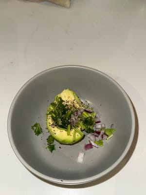 In einer Schüssel die Avocado mit roten Zwiebeln, Koriander, Zitronensaft und schwarzem Pfeffer glatt pürieren. Für eine cremigere Konsistenz einen zusätzlichen Esslöffel griechischen Joghurt hinzufügen (optional).