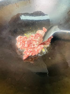 Für die Basisaromen anbraten: Öl in einer Pfanne bei schwacher Hitze erhitzen, zerdrückte Knoblauchzehen und Ingwerscheiben hinzufügen und anbraten, bis sie duften (für eine leichtere Konsistenz können Sie die Knoblauchzehen entfernen; ansonsten in der Pfanne lassen).

Hackfleisch hinzufügen und von beiden Seiten goldbraun anbraten, dabei das Fett auslassen. Einen kleinen Löffel weißen Pfeffer hinzufügen, dann einen Löffel Kochwein am Pfannenrand entlang träufeln und gleichmäßig braten.