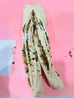 用切面刀在中间切一刀,向外翻一下,把有肉松的一侧朝上,再交叉卷起来,收口朝下,放进吐司盒里准备二次发酵。