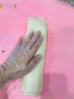 Menggulung adonan
Gulirkan adonan yang sudah dilapisi menjadi lembaran selebar 5 cm. Rapatkan sisi dan ujung gulungan agar tidak berubah bentuk saat dipanggang. Tekan adonan perlahan dengan tangan Anda agar isian lebih mudah menempel.