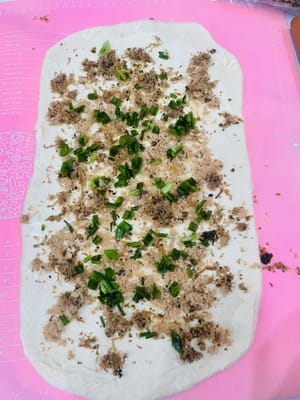 Mengoles dan Menaburkan
Olesi adonan yang sudah digulung dengan saus salad, taburi dengan abon babi dan daun bawang cincang, lalu jika suka keju, taburi keju parut di atasnya, seperti membuat topping pizza.