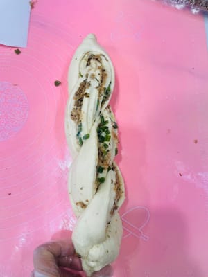 用切面刀在中间切一刀,向外翻一下,把有肉松的一侧朝上,再交叉卷起来,收口朝下,放进吐司盒里准备二次发酵。
