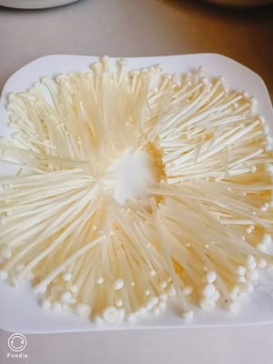 Geschredderte Enoki-Pilze auf einen Teller geben.
