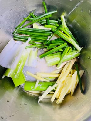 次に、ネギのセグメントとショウガのスライス（手で魚臭さを取り除くための材料）を洗って刻み、ボウルに入れ、冷ました熱湯50mlを加え、風味が出るまで力強くこすります（目的：ネギとショウガ自身の香りを利用して魚臭さを「こすり出す」ため、直接浸すよりも効果的です）。